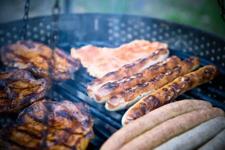 Close-up of various meats including sausages grilling outdoors on a barbecue.